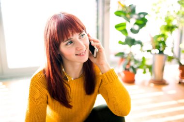 Kızıl saçlı kadın ev ofisinden telefon ediyor. Şehirdeki dairesinden uzaktan çalışan iş kadını..