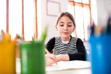 Masada oturup yazı yazan tatlı bir kız portresi. İlkokulda sınıf öğrencisi..