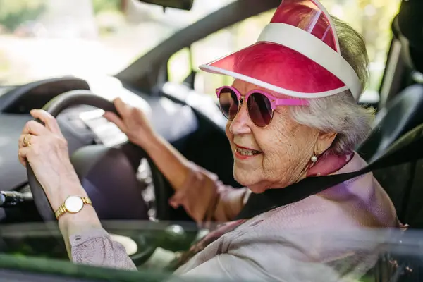 stock image Happy senior woman driving car alone, enjoying the car ride. Safe driving for elderly adults, older driver safety. Driving license renewal at older age.