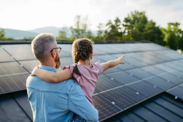 Stock image Rear view of father with girl on roof with solar panels, hugging. Rooftop solar or photovoltaic system. Sustainable future for next generation concept.