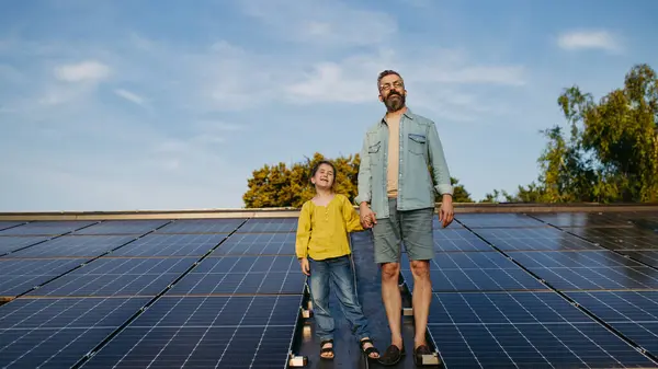 stock image Father standing with girl on roof with solar panels, holding hands. Rooftop solar or photovoltaic system. Sustainable future for next generation concept.