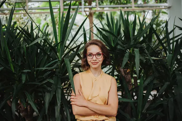 stock image Businesswoman selling flowers and seedlings, standing in greenhouse, looking at camera, smiling. Small greenhouse business.