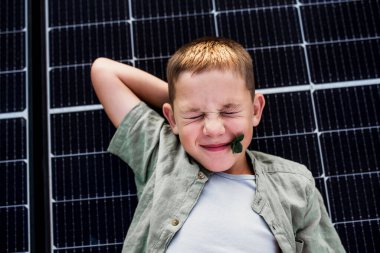 Top view of boy lying on roof with solar panels, looking at camera. Sustainable future for next generation concept. clipart