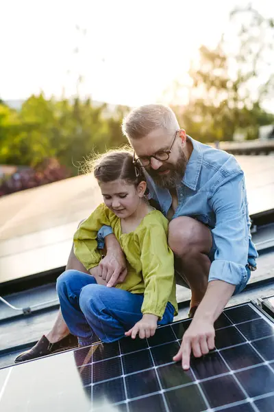 stock image Dad and girl on roof with solar panels, learning about solar energy. Rooftop solar or photovoltaic system. Sustainable future for next generation concept.