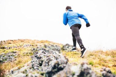 Erkek koşucu, tepeden yukarı toprak koşu yolunda doğada koşuyor. Genç adam için sabah koşusu eğitimi.