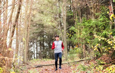 Erkek koşucu tepenin aşağısındaki ormanda koşuyor. Genç adam için sabah koşusu eğitimi.