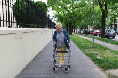 Güzel, yaşlı bir kadın rollatörle sokakta yürüyor, markete alışverişe gidiyor..