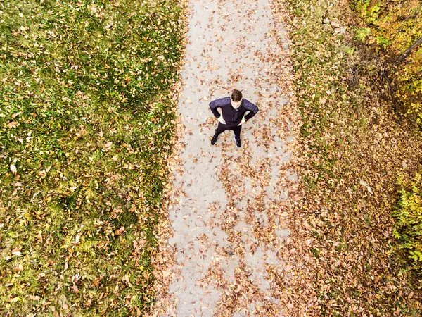 stock image Aerial view of a runner standing on jogging path with fallen leaves and resting after in autumn park. Morning running training for man.