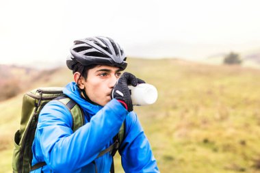 Genç bisikletçi, güzel bir sonbahar sabahının ortasında şişeden su içiyor ve dinleniyor. Aktif ve sağlıklı yaşam tarzı kavramı.