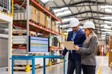 Kadın mühendis ve erkek proje yöneticisinin modern endüstriyel fabrikada dikey görüntüsü, üretimden bahsediyor. Üretim tesisinde takım yönetimi