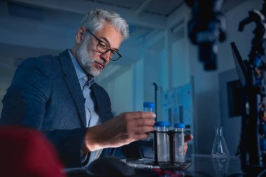 Male scientist in the laboratory holding test tubes and intently looking at its contents. clipart