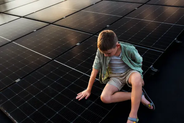 stock image Boy sitting on roof with solar panels, touching panel with hands. Sustainable future for next generation concept.