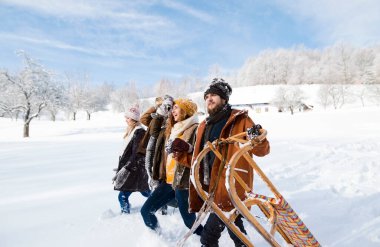 Group of friends pulling sleds behind them, going to sleddingin in snowy nature. First snow of the season clipart