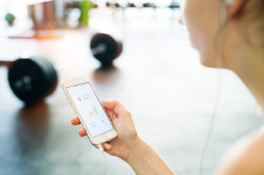 Genç fitness kızı spor salonunda sıkı çalıştıktan sonra smatphone 'da performansını kontrol ediyor..