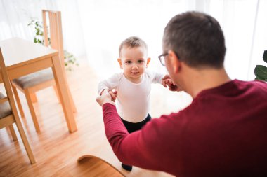Babası küçük oğluyla oynuyor, elini tutuyor, ilk adımlarına yardım ediyor..
