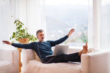 Evdeki adam dizlerinde dizleriyle koltukta oturuyor, kulaklıkları başında, meditasyon müziği dinliyor.