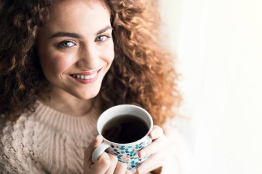 Sabah kahvesi. Yatağında kıvırcık saçlı, kahve içen güzel bir genç kadın..