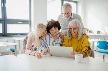 Tablet ekranına bakan bir grup son sınıf öğrencisi yeni yetenekler öğreniyor. Bilgisayar ve teknoloji eğitimine katılan yaşlılar.