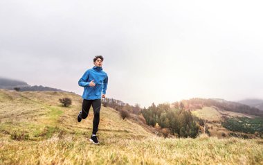 Erkek koşucu, toprak yolda doğada koşuyor. Genç adam için sabah koşusu eğitimi.