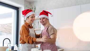 Young man with Down syndrome and his mom dancing while baking Christmas gingerbread cookies in kitchen. clipart