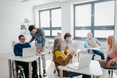 Öğretmen son sınıf öğrencilerine laptopla ve internetle nasıl çalışacaklarını anlatıyor. Bilgisayar ve teknoloji eğitimine katılan yaşlılar.