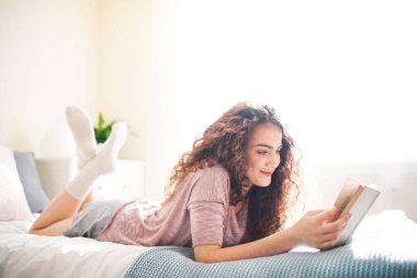 Kıvırcık saçlı, yatakta uzanmış kitap okuyan güzel bir kadının portresi..