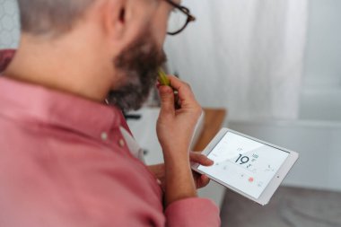 Adam banyoda dişlerini fırçalarken termostat kullanıyor. Ev ısıtma ve termostatlarında sürdürülebilir, verimli ve akıllı teknoloji kavramı.