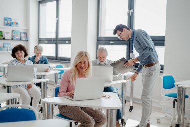 Öğretmen son sınıf öğrencilerine laptopla ve internetle nasıl çalışacaklarını anlatıyor. Bilgisayar ve teknoloji eğitimine katılan yaşlılar.
