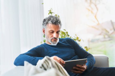 Evdeki adam, tablette TV programı izliyor, kanepede oturuyor..