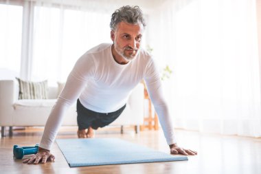 Evde spor paspası üzerinde egzersiz yapan yakışıklı bir adam, şınav çekiyor. Orta yaşlı bir adam için rutin ev çalışması.