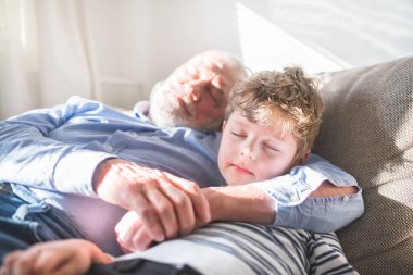 Oğlan ve büyükbaba kanepede kestiriyorlar. Büyükbaba torunuyla vakit geçirir, ailesi işteyken ona bakar.