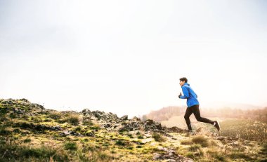 Erkek koşucu, toprak yolda doğada koşuyor. Genç adam için sabah koşusu eğitimi.