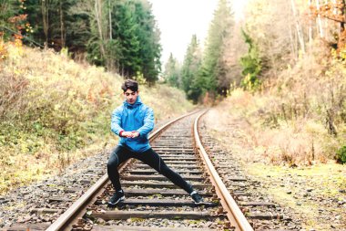 Sportif adam doğanın ortasında kullanılmamış raylar üzerinde egzersiz yapıyor. Genç adam için sabah antrenmanı.