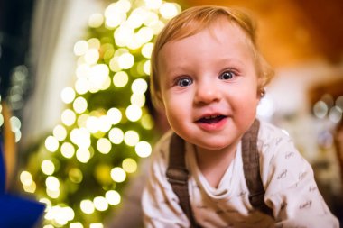 Little baby boy in Christmas home. Cute boy is surprised and amazed by Christmas decorations. clipart