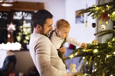 Babam Noel ağacını Noel evinde küçük oğluna gösteriyor. Sevimli erkek bebek yılbaşı süslemelerine hayran kaldı.