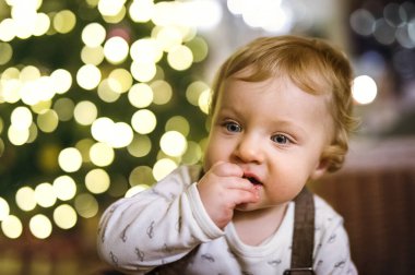 Little baby boy in Christmas home. Cute boy eating christmas cookies by Christmas tree in living room clipart