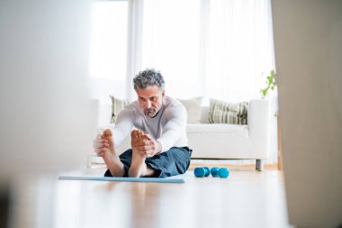 Yakışıklı adam evde spor paspası üzerinde egzersiz yapıyor, yoga yapıyor, esneme hareketleri yapıyor. Orta yaşlı bir adam için rutin ev çalışması.