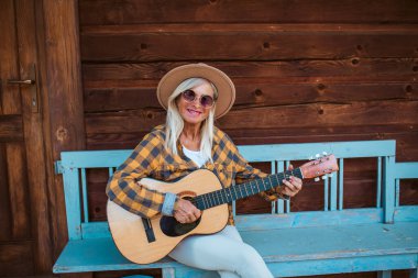 Güzel yaşlı kadın kamarasının önünde oturuyor, gitar çalıyor.