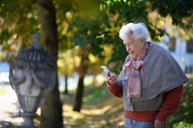 Parktaki yaşlı kadın, elinde akıllı telefon ve mesajları tutuyor..
