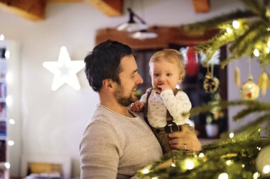 Father showing christmas tree to little son in Christmas home. Cute baby boy is amazed by christmas decoration clipart