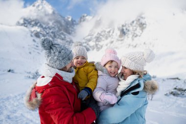 Aile dağlarda kış tatilinin tadını çıkarıyor. Karlı bir arazinin ortasında duruyor..