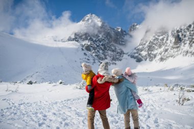 Karlı bir arazinin ortasında duran aile manzarası, dağlarda kış tatilinin tadını çıkarıyor..