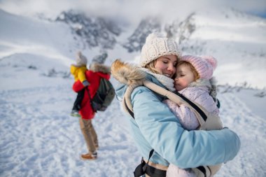 Aile dağlarda kış tatilinin tadını çıkarıyor. Karlı bir arazinin ortasında duruyor..