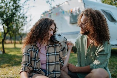 Genç çift doğada kamp gezisinde köpekle oynuyor, kampçının önünde oturuyor. Kervan gençler için yola çıktı.