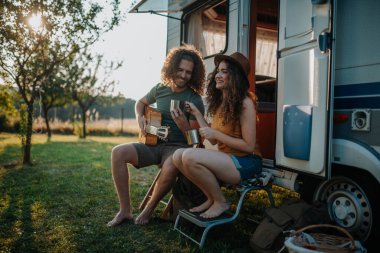 Karavanın yanında oturan çift, gitar çalan adam ve dizüstü bilgisayarda çalışan kadın..
