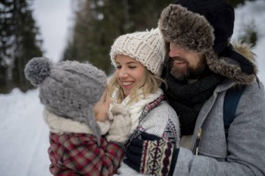 Aile dağlarda kış tatilinin tadını çıkarıyor, karlı ormanın ortasında duruyor..