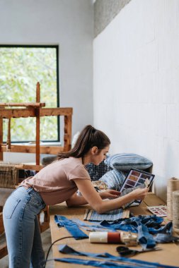 Young businesswoman working on workbench, preparing old fabric for weaving. Upcycled textile, small cloth weaving business and circular economy. clipart