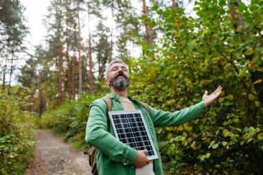 Handsome man standing in the middle of forest, holding small solar panel above his head clipart