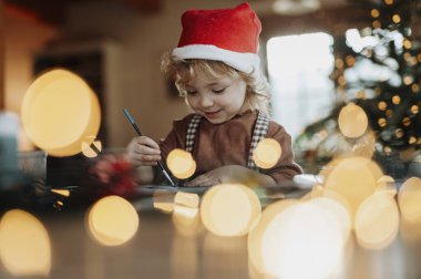 Noel evinde küçük bir kızın portresi, Noel Baba için resim yapmak ya da Noel süsü yapmak..