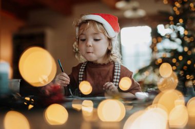 Noel evinde küçük bir kızın portresi, Noel Baba için resim yapmak ya da Noel süsü yapmak..